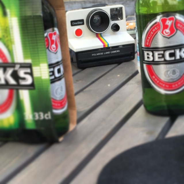 several beers, two with cameras and a polaroid are lined up on a table