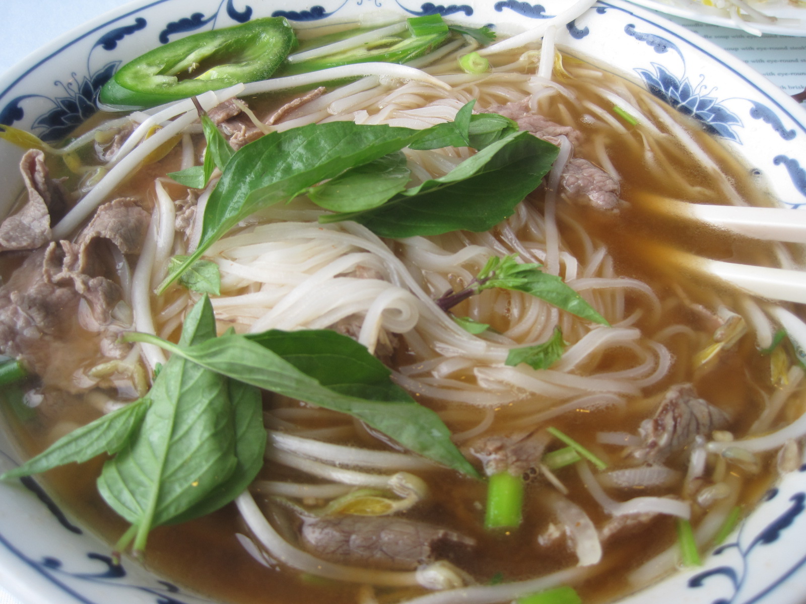 bowl of asian noodle soup with herbs and meat