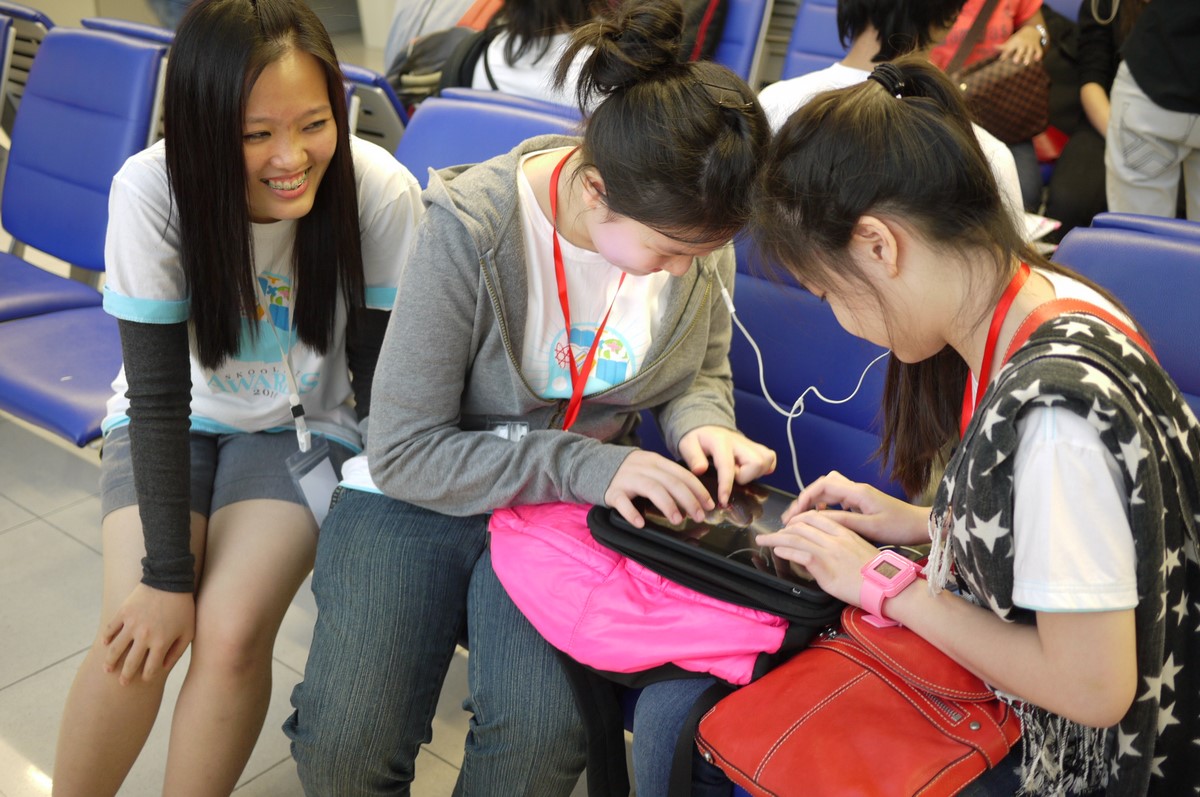 three girls sitting down, one using her cell phone