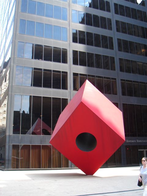 a sculpture of a red cube next to an office building