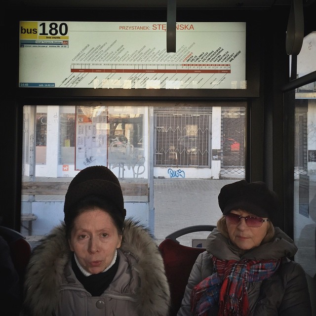 two women sitting in front of a bus window with a building and street sign behind them