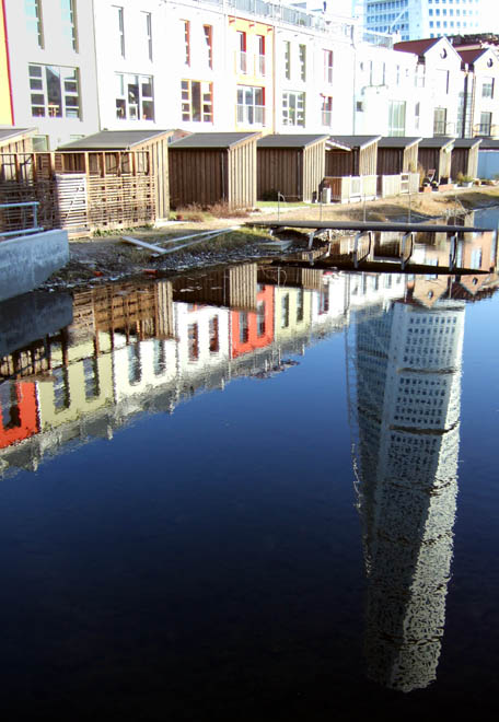 buildings are reflected in a calm waterway on a sunny day