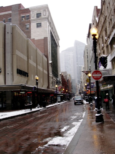 a street scene with snow on the ground and buildings