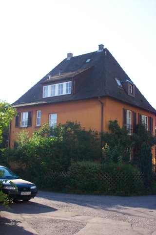 a yellow house with windows, shrubs and parked car