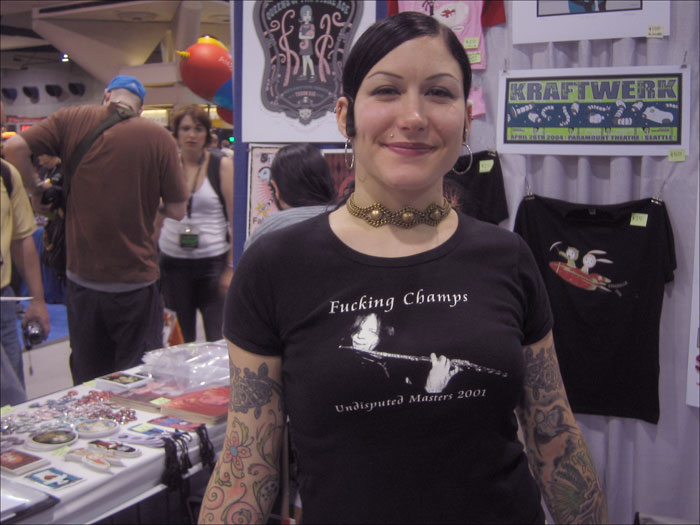 a woman with lots of tattoos smiling in front of a stand