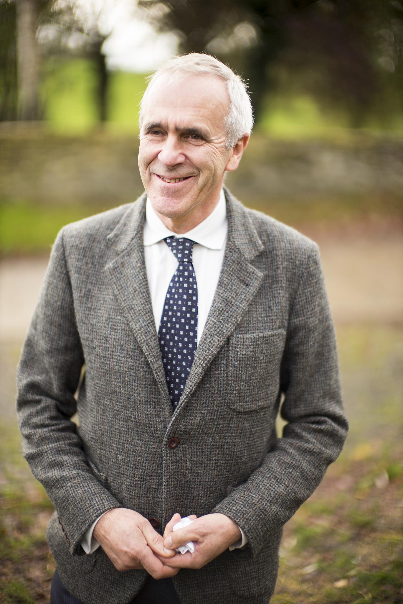 a older gentleman in a suit and tie standing smiling