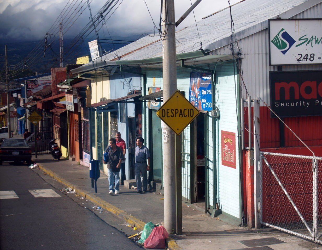 pedestrians and cars waiting outside a store on a sidewalk