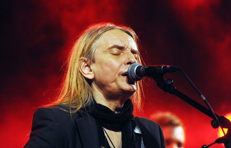 a man with long hair and a suit on is playing a guitar