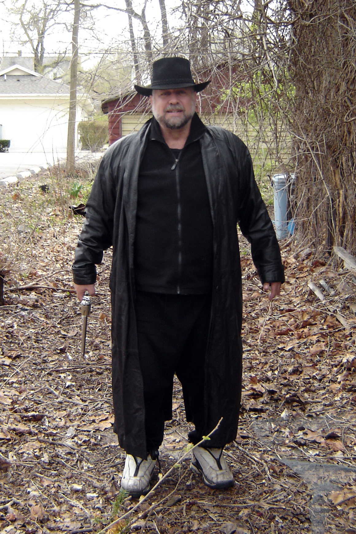 a man in a costume with a hat and tie stands in leaves