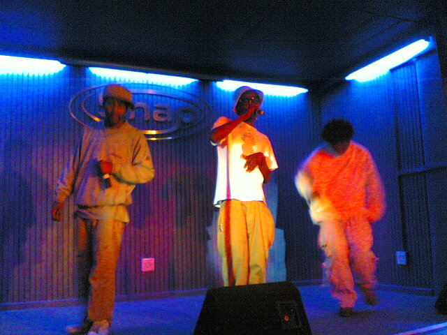 three men in bright costumes stand on stage