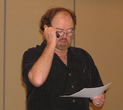 a man with glasses, black shirt and beard talks on a cell phone