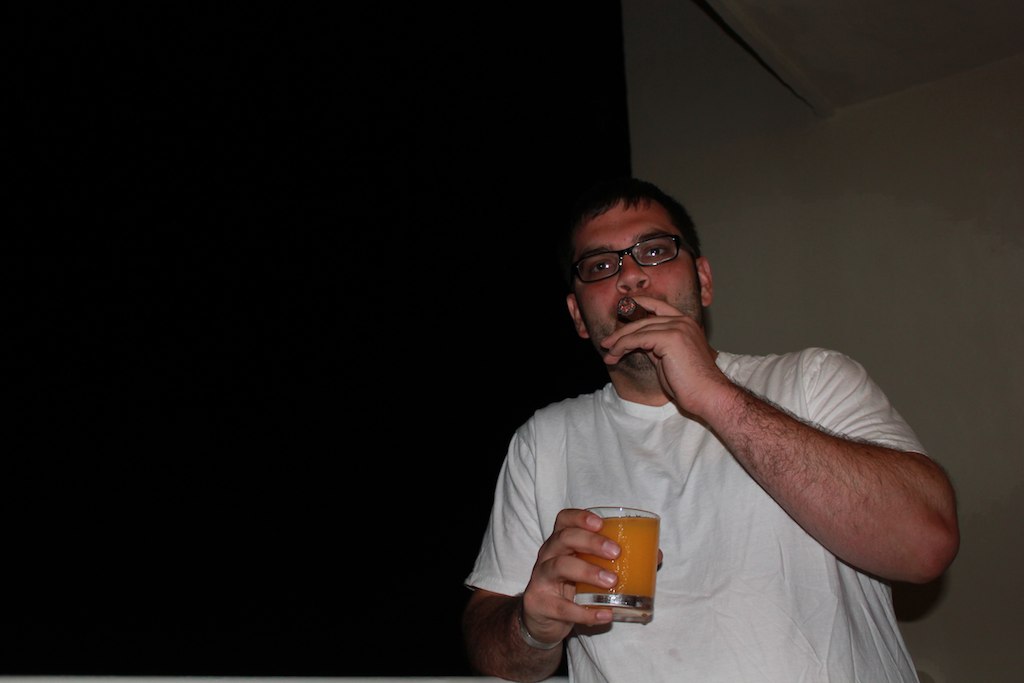 man drinking a glass of orange juice while standing in a dark room