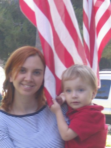 woman holding child next to giant american flag