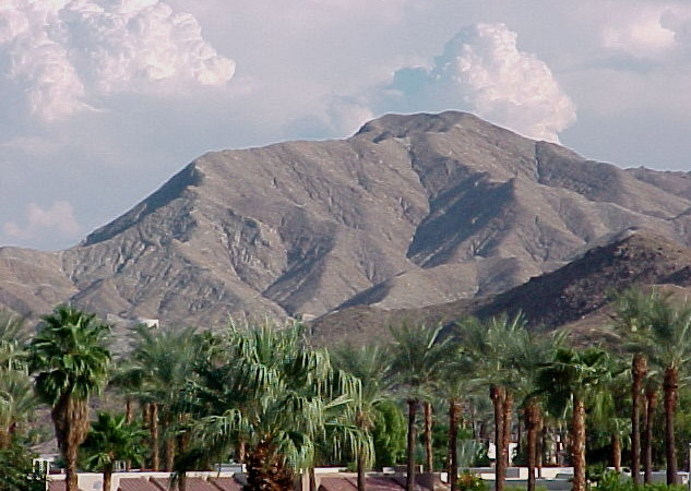 large brown mountains surrounded by palm trees and a cloudy sky