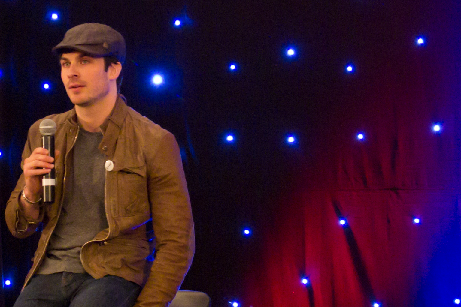 a male in a brown jacket some blue lights and a microphone