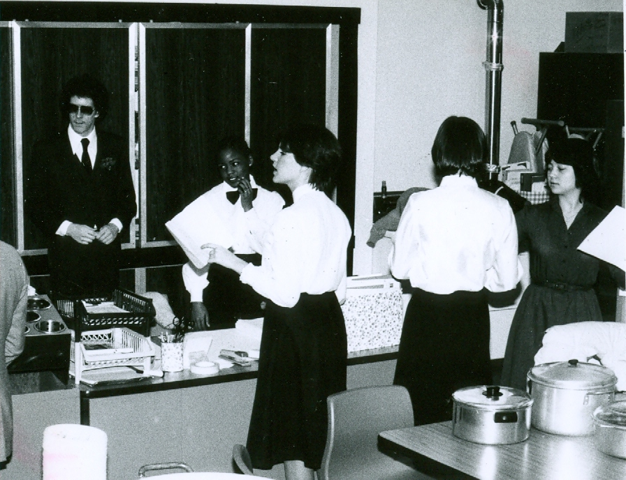 several young men wearing white shirts and black pants, and other men in ties are standing near the counter