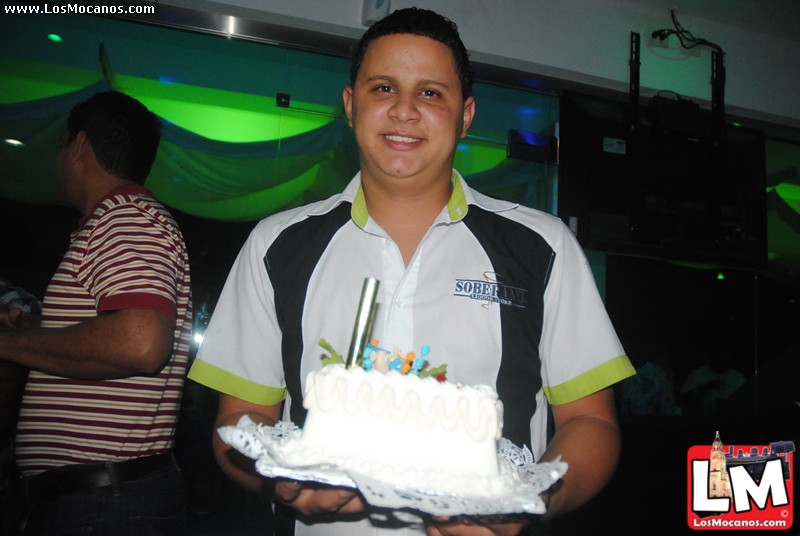a smiling man in striped shirt holding a white cake