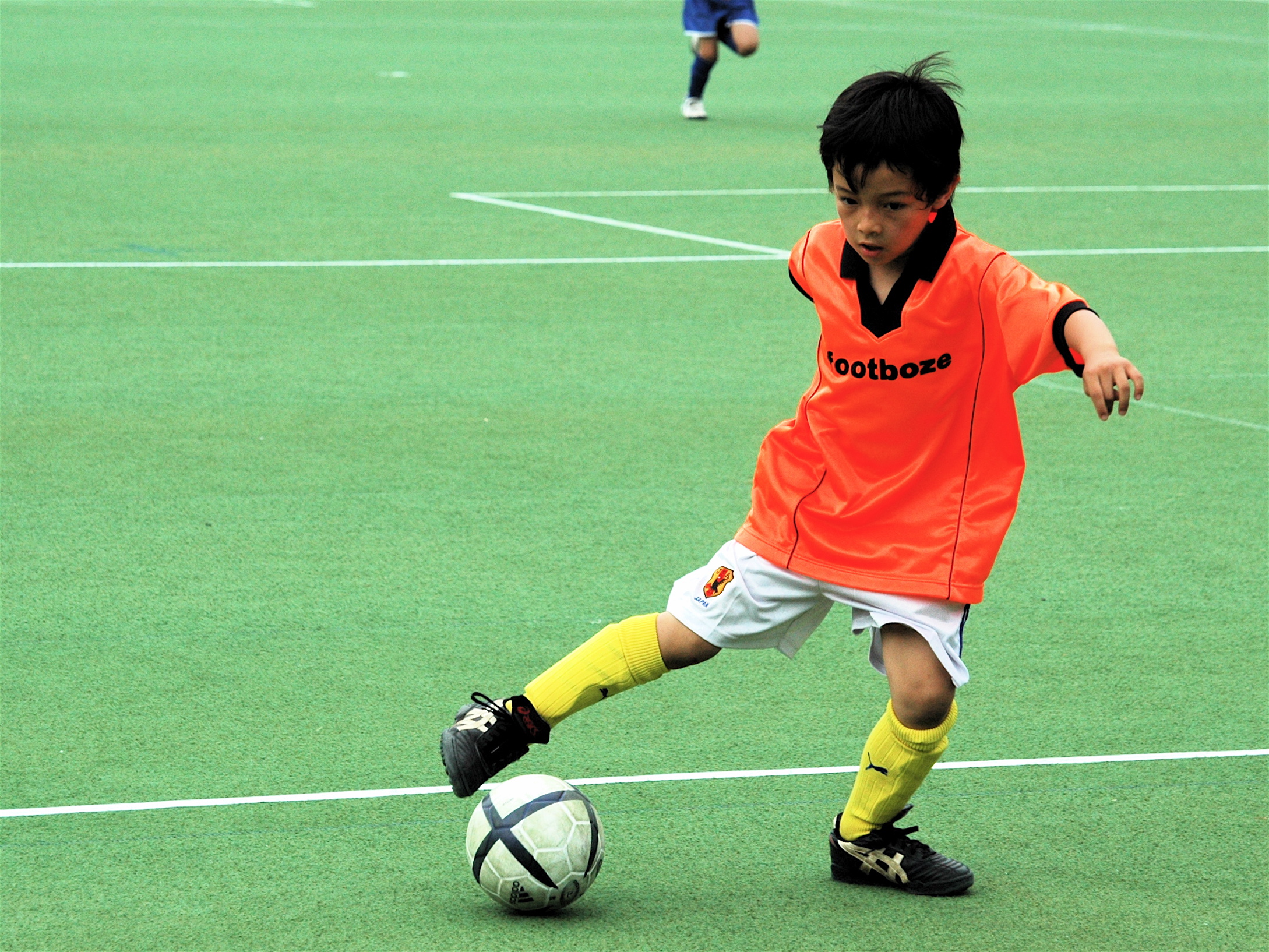 a child wearing an orange soccer shirt dribbles a soccer ball