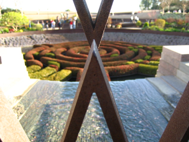 the view from behind a piece of metal looking towards an elaborate garden