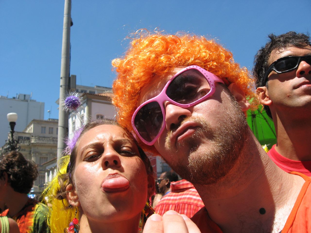 a man with an orange afro and pink sunglasses next to two women