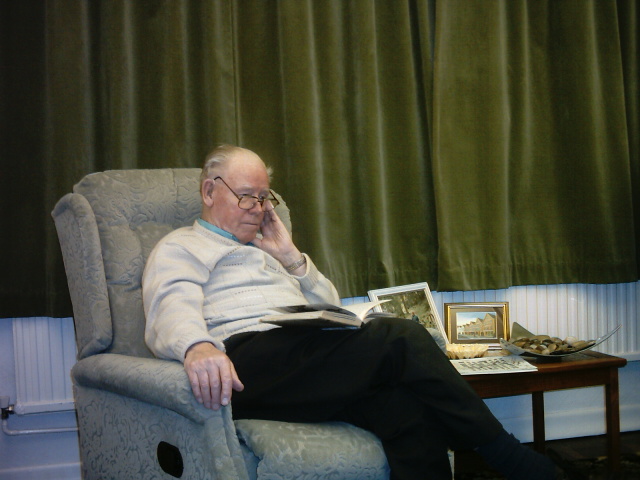 man in white sweater sitting in chair holding cell phone to his ear