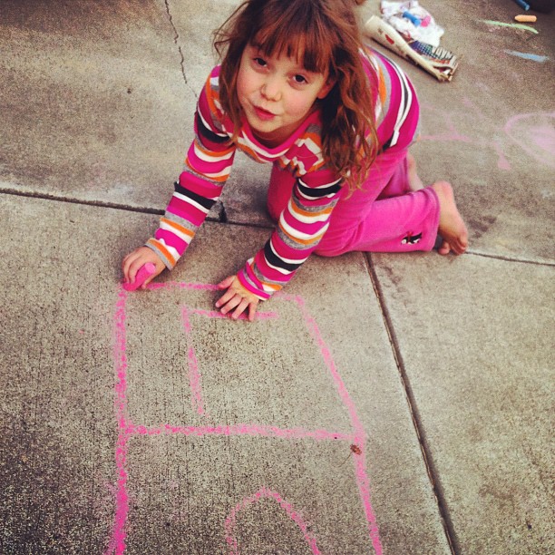 a little girl playing in the sidewalk with chalk