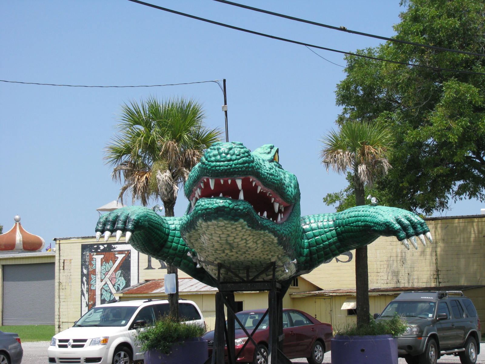 a large green alligator statue sitting in front of cars