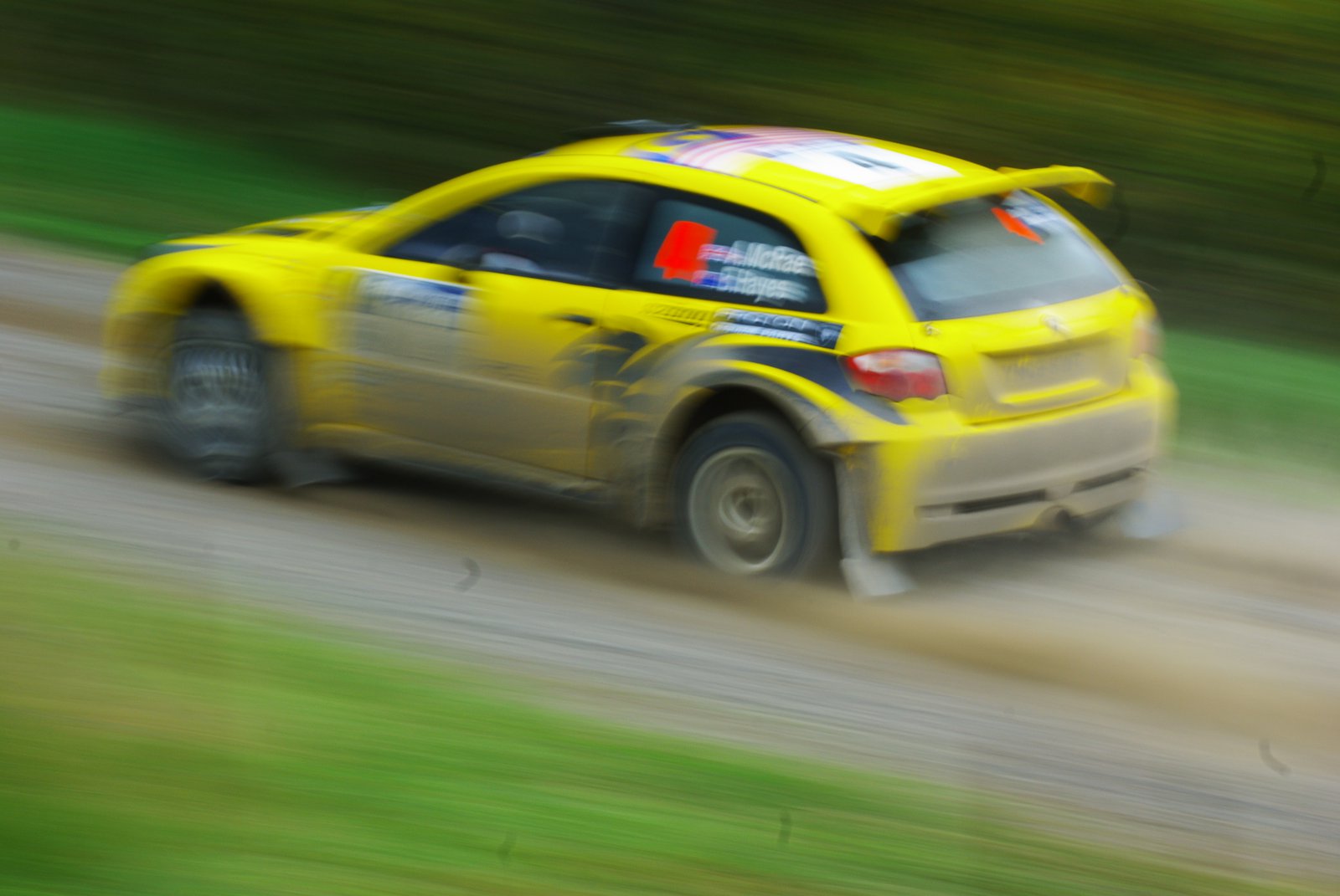 a small yellow car with yellow stickers drives along a dirt road