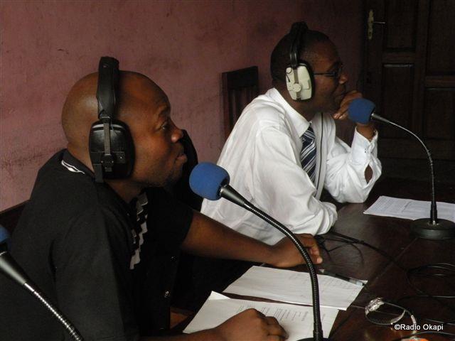 two men are sitting at a desk while holding microphones