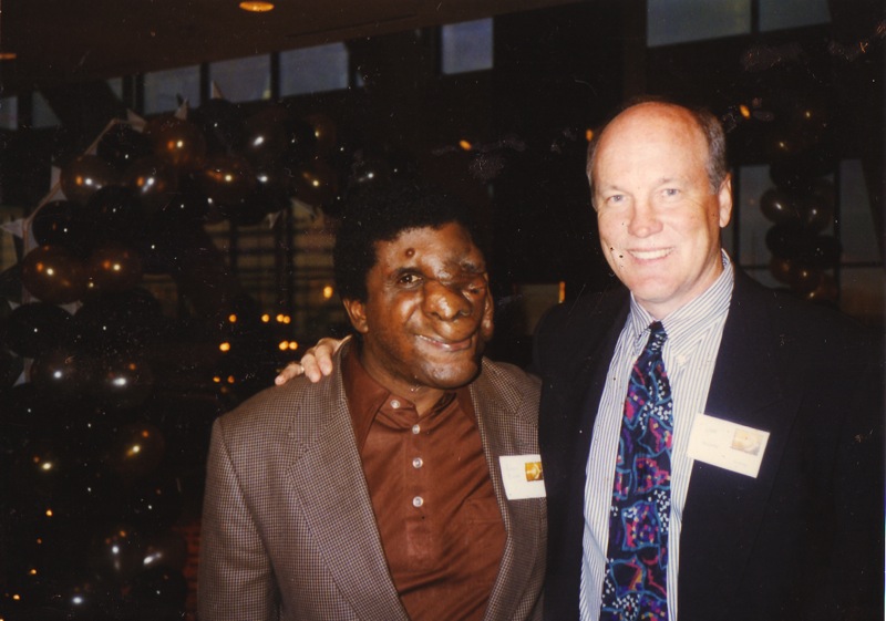 a man with a blue and white striped tie stands next to another man