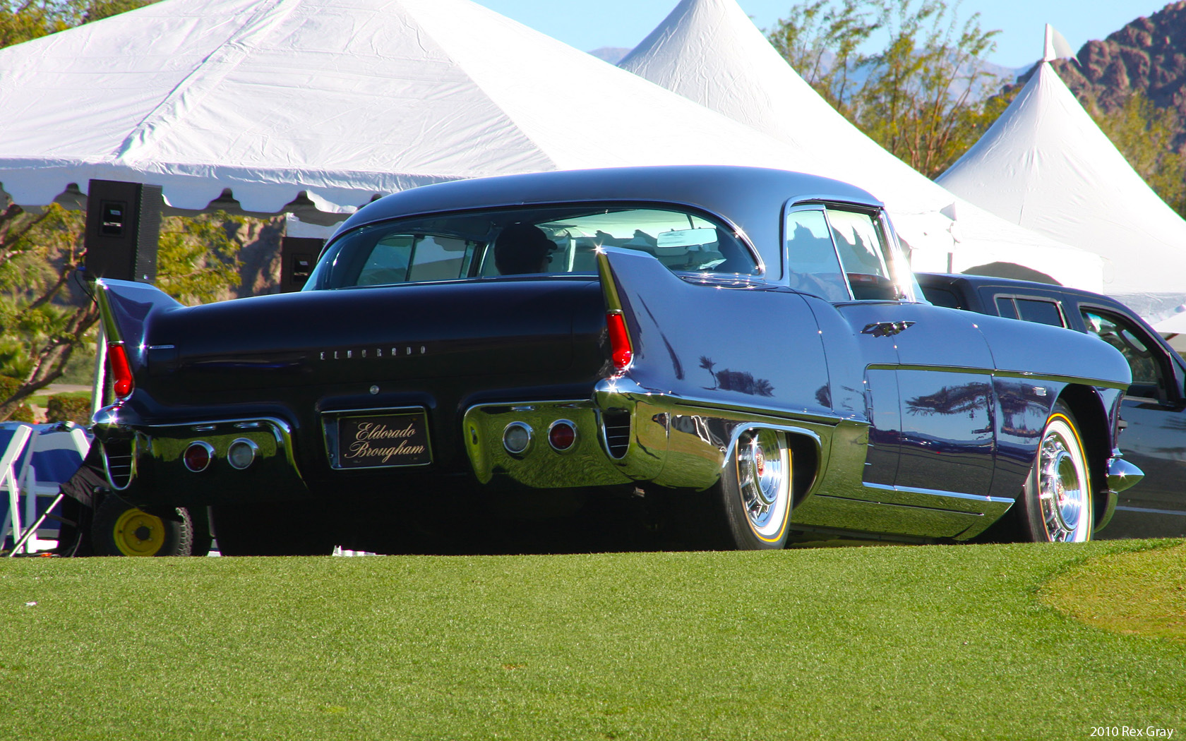 a large classic car on the grass by some tents