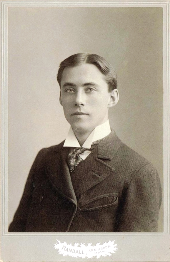 an antique black and white pograph shows a young man in a sweater and tie