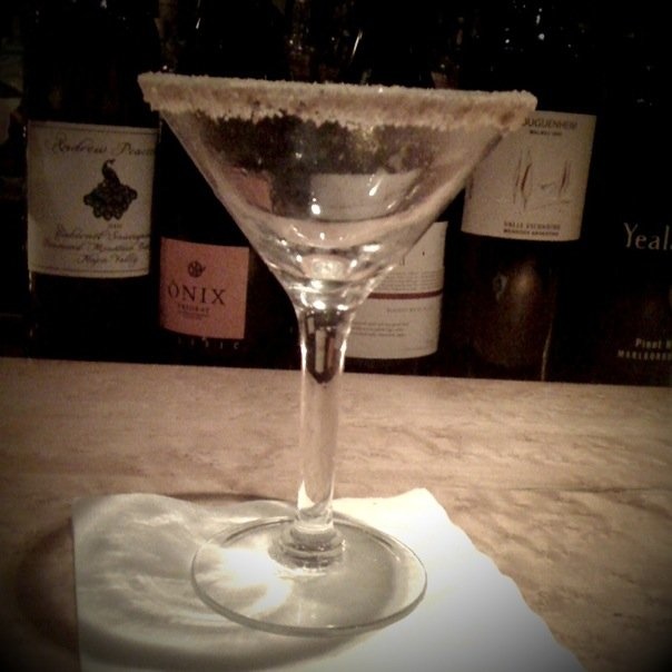 a picture of a partially filled martini with the wine bottles behind it