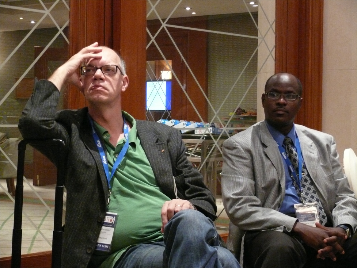 two men sitting in a chair and one has a cellphone