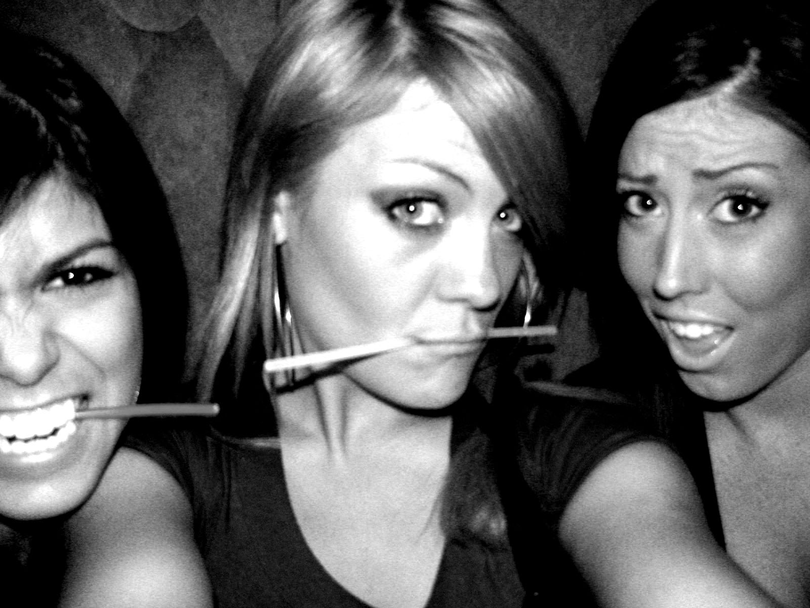 three women smiling while brushing their teeth in front of the camera