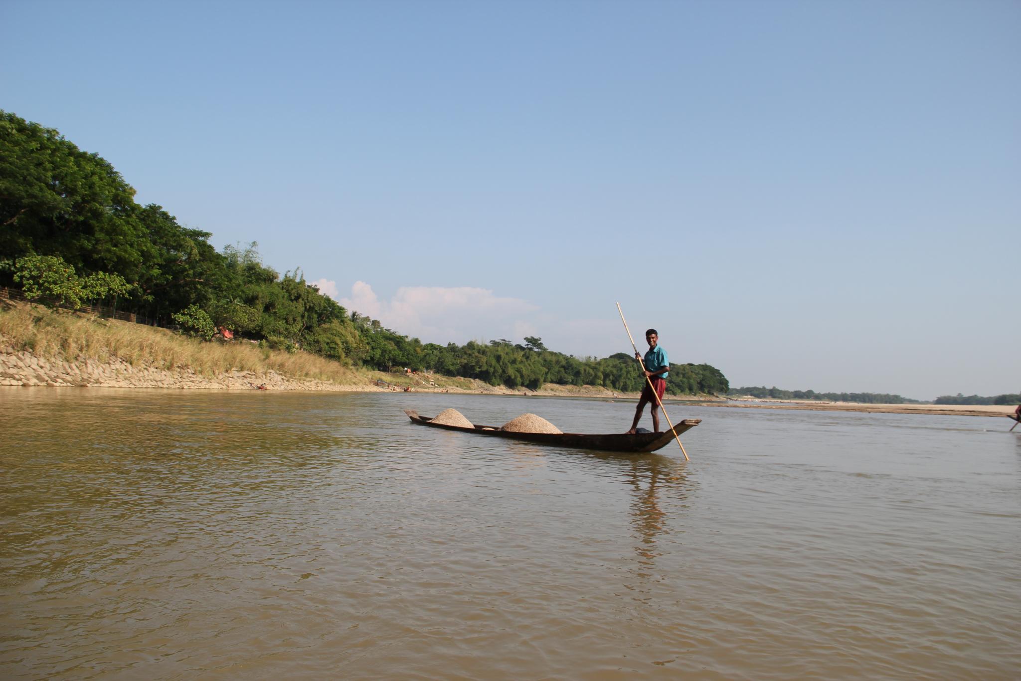 a man with a pole stands on a river while rowing a canoe