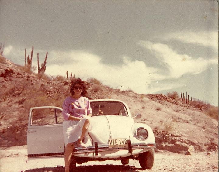 a woman is posing next to a car on the dirt