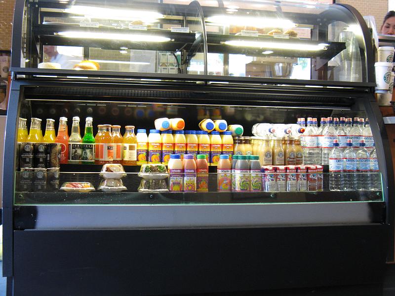 a display case full of bottled beverages in front of a food stand