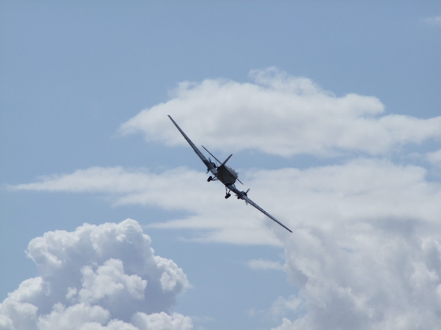 a large airplane flying over the clouds on a blue sky