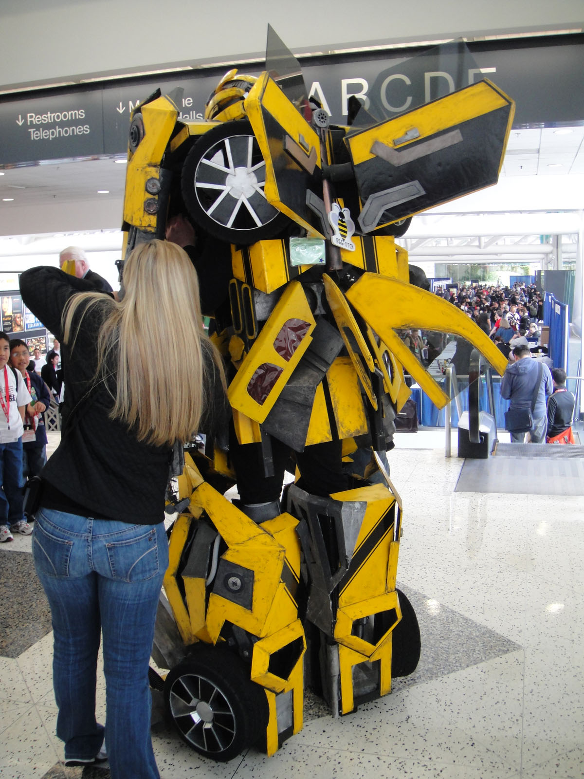 woman leaning up against an enormous yellow robot with wheels