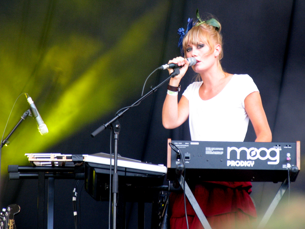 a woman is standing at a keyboard on stage with her microphone in front of a microphone on her lap