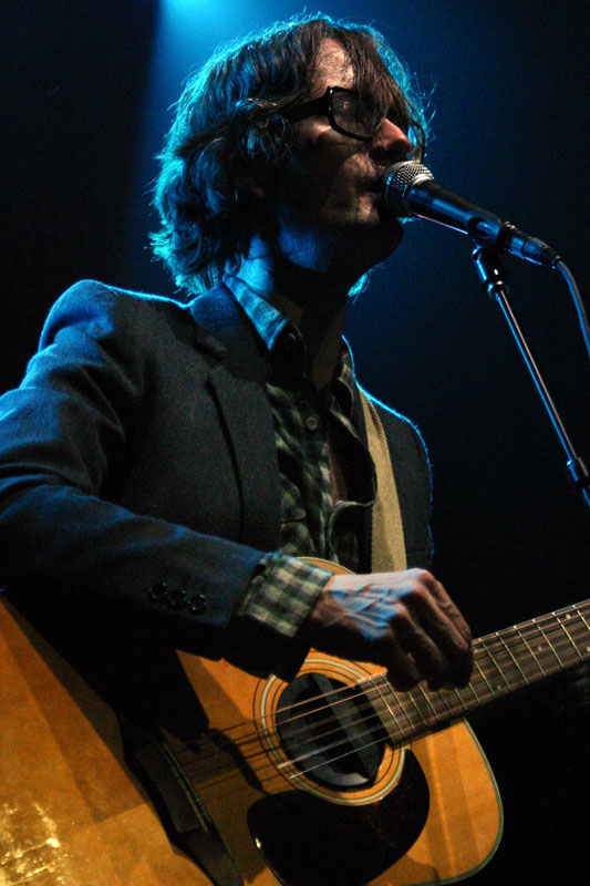 a man with long hair and glasses, playing a guitar