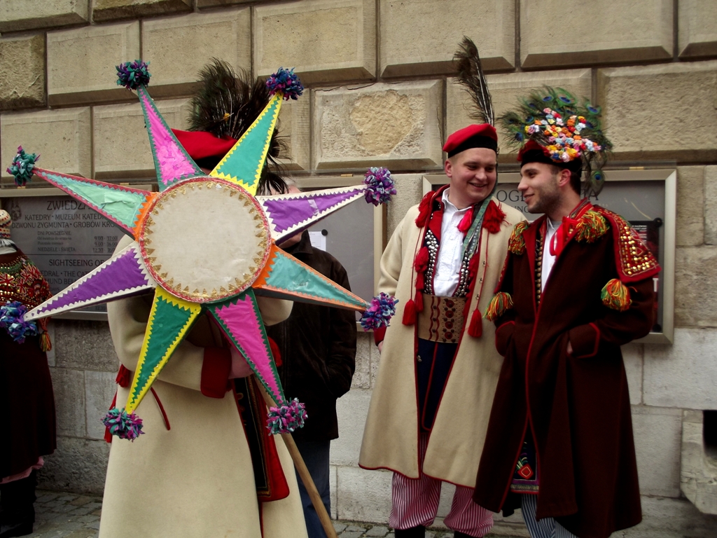 two men dressed in colorful traditional costume and headdress standing by the side of a building with a star