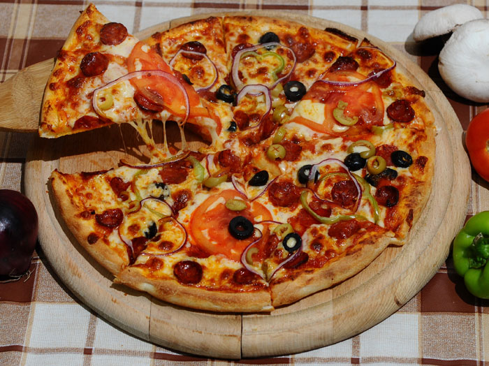 a pizza on a pizza stone with peppers and pepperoni