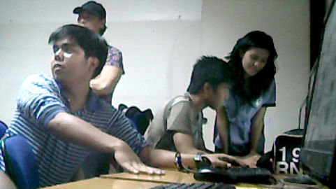 three young adults are working at a computer in a room with chairs