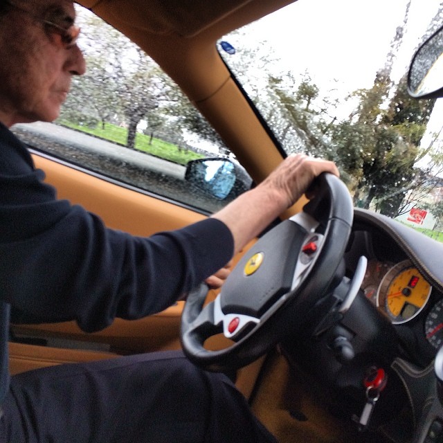 a man wearing glasses driving on the front of a yellow car