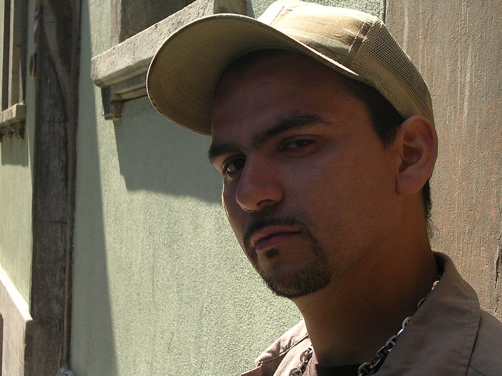 man wearing hat looking directly at camera, standing next to building