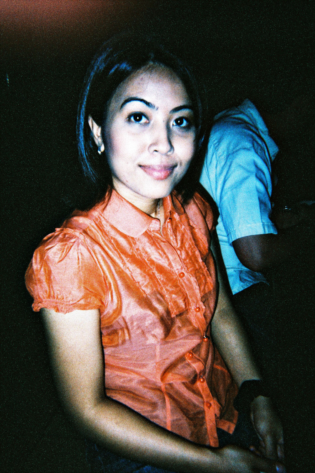 a woman sitting down in front of a camera with another woman in the background