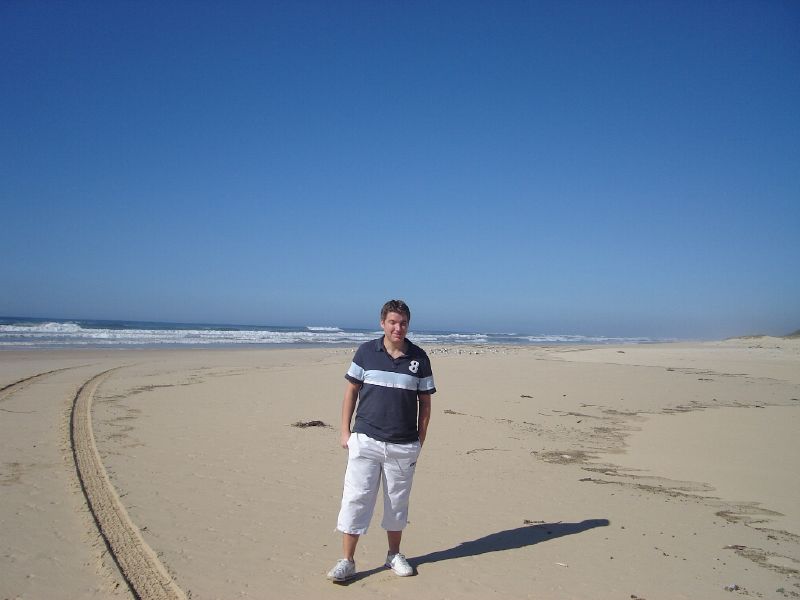 a man in grey shirt standing on beach next to sand