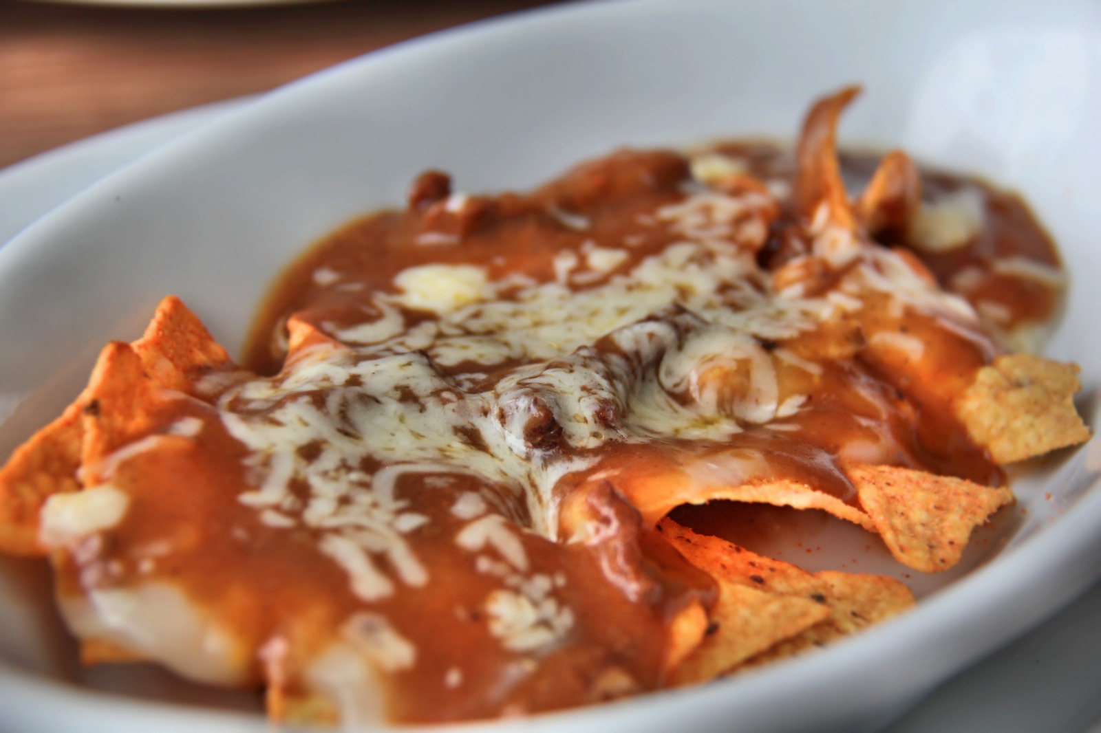 a white bowl with nachos topped with red sauce